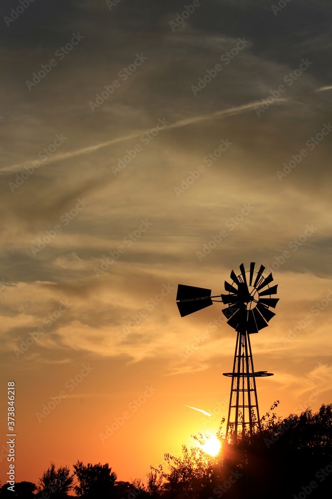 Kansas Sunset with a colorful sky and clouds with a Windmill silhouette north of Hutchinson Kansas USA.
