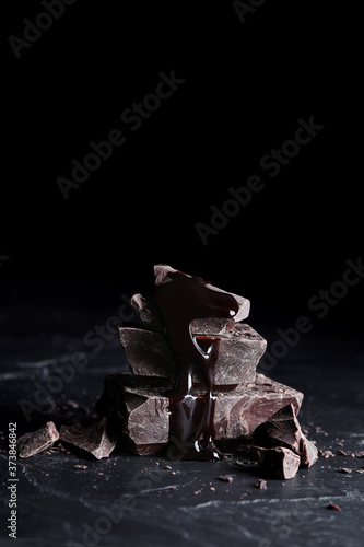 Pieces of tasty dark chocolate with syrup on black table, closeup. Space for text