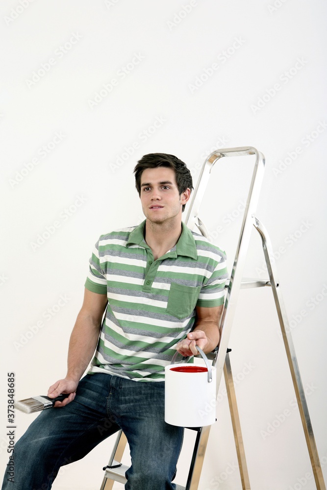 Man holding a bucket of paint and paintbrush, sitting on a ladder Man holding a bucket of paint and paintbrush, sitting on a ladder
