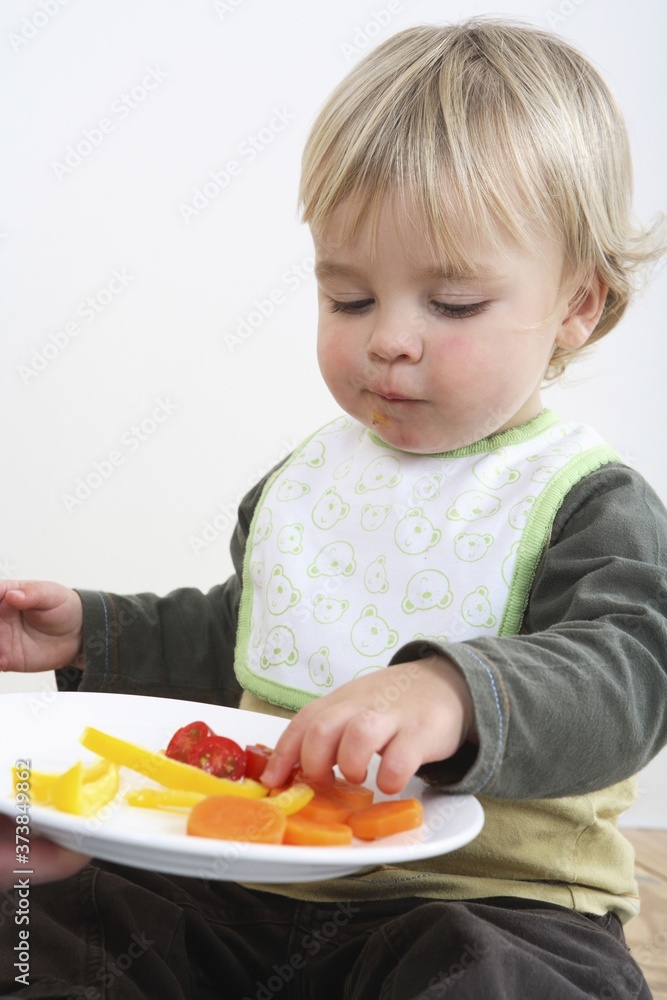 Preschooler with baby bib eating vegetables Preschooler with baby bib eating vegetables
