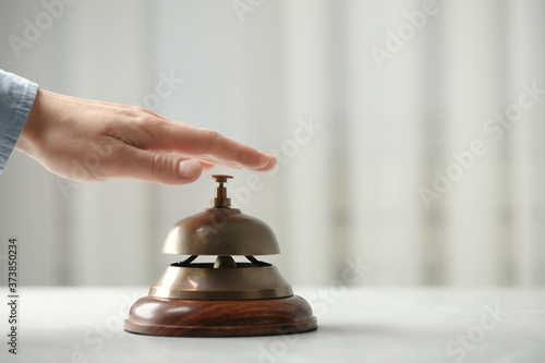 Man ringing hotel service bell at table indoors, closeup. Space for text