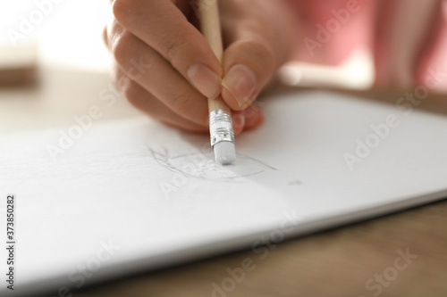 Woman correcting picture in notepad with pencil eraser at table, closeup