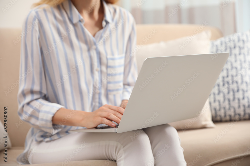 Fototapeta premium Young woman with laptop sitting on sofa indoors, closeup