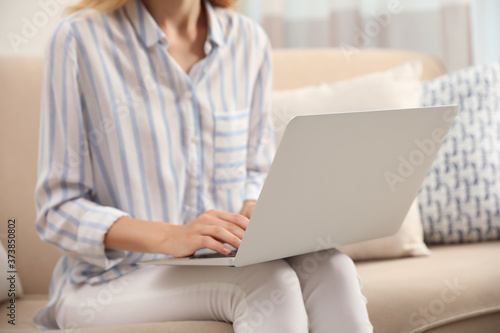 Young woman with laptop sitting on sofa indoors, closeup