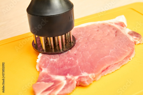Piece of pork and meat tenderizer on cutting board photo