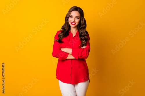 Photo of pretty curly business lady bright pomade bossy person friendly smiling teeth arms crossed wear office red shirt white trousers isolated yellow vivid color background