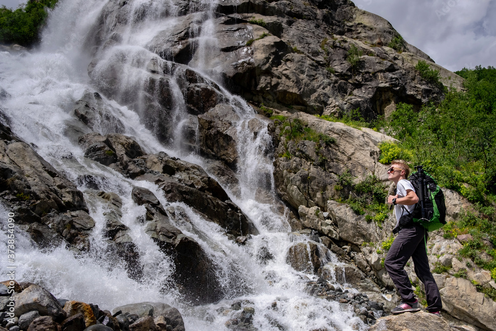 Man hiking with backpack looking at waterfall. Portrait of male adult back standing outdoor. Man hiking with backpack looking at waterfall. Portrait of male adult back standing outdoor.