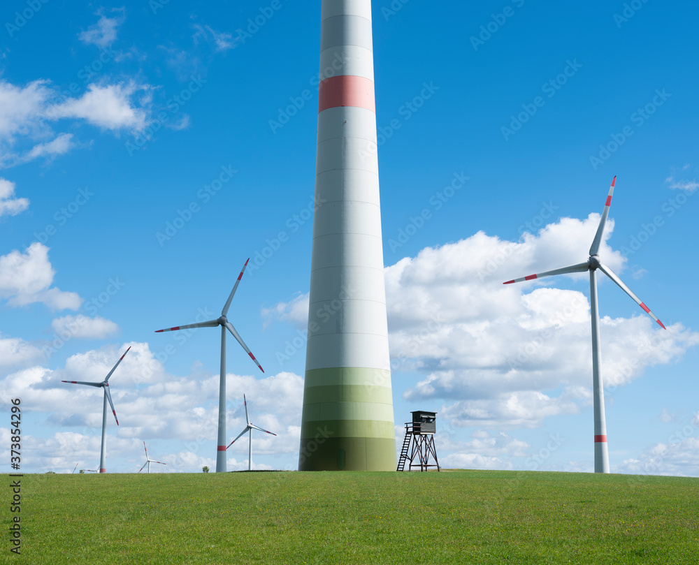 wind turbines and high seat in german eifel in green grass with blue sky and white clouds wind turbines and high seat in german eifel in green grass with blue sky and white clouds