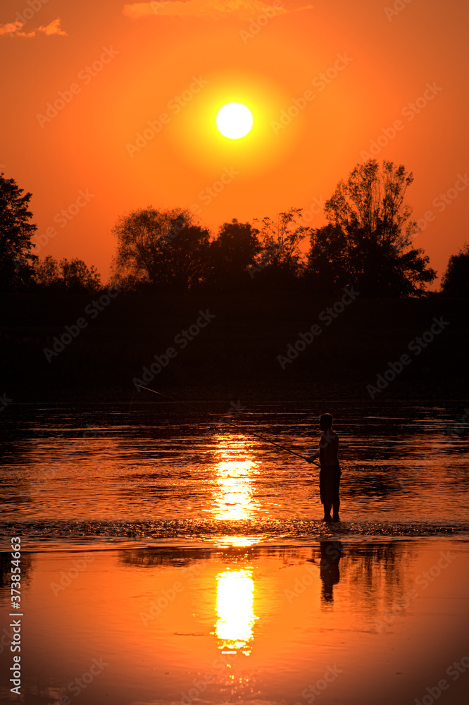Fisherman fishing at sunset, sun reflecting in water Fisherman fishing at sunset, sun reflecting in water