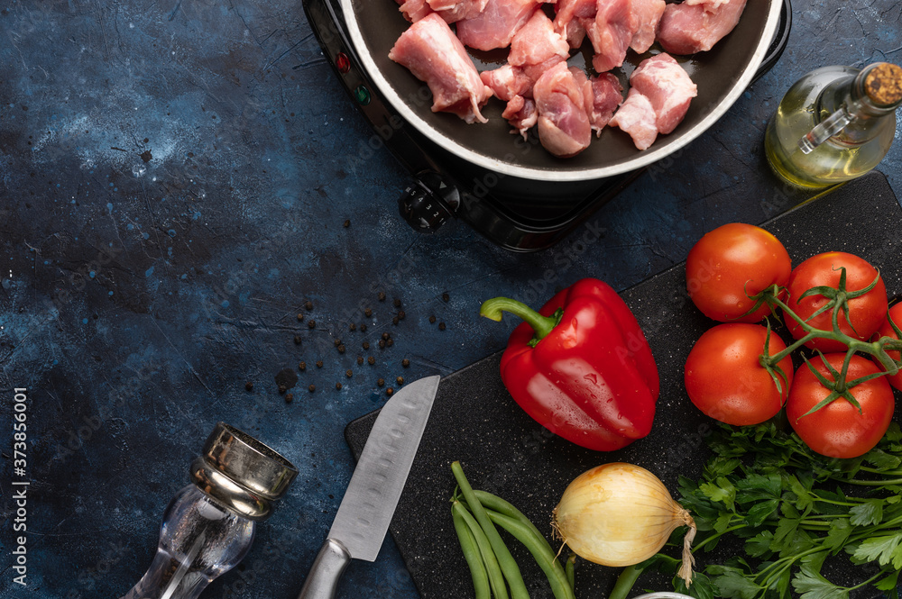 Fresh pork is fried in a skillet on a background of vegetables, with space for an inscription, cooking and a book of recipes Fresh pork is fried in a skillet on a background of vegetables, with space for an inscription, cooking and a book of recipes
