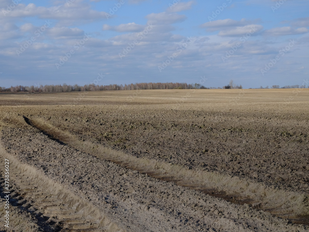 Traces of large agricultural machinery in a plowed field. The sky over the farmland. Agricultural landscape. Traces of large agricultural machinery in a plowed field. The sky over the farmland. Agricultural landscape.