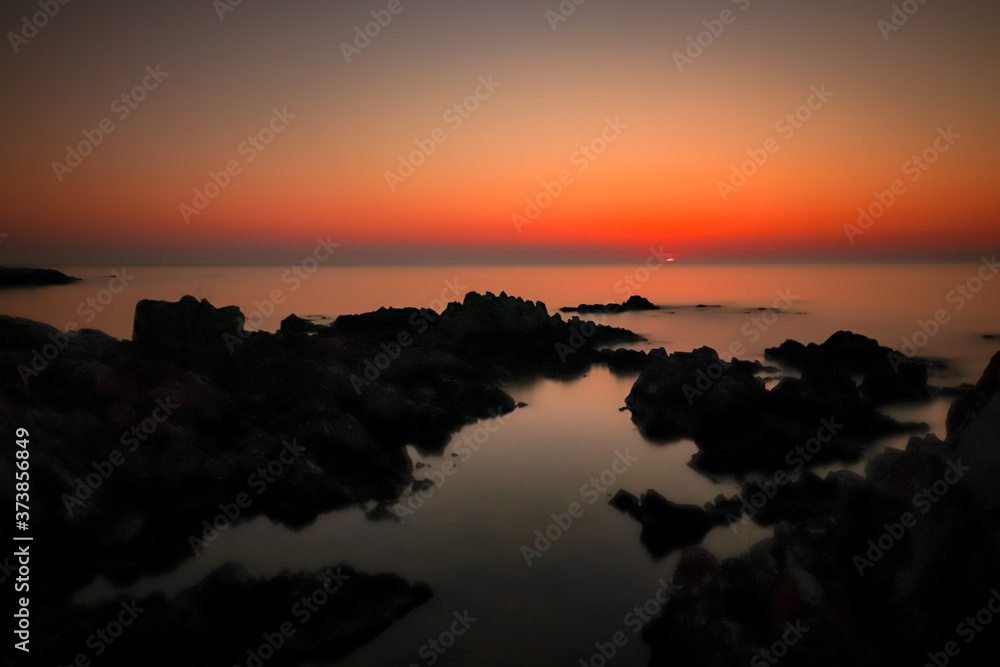 Sonnenaufgang über dem Wasser mit Felsen und Spiegelung
