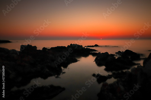 Sonnenaufgang über dem Wasser mit Felsen und Spiegelung