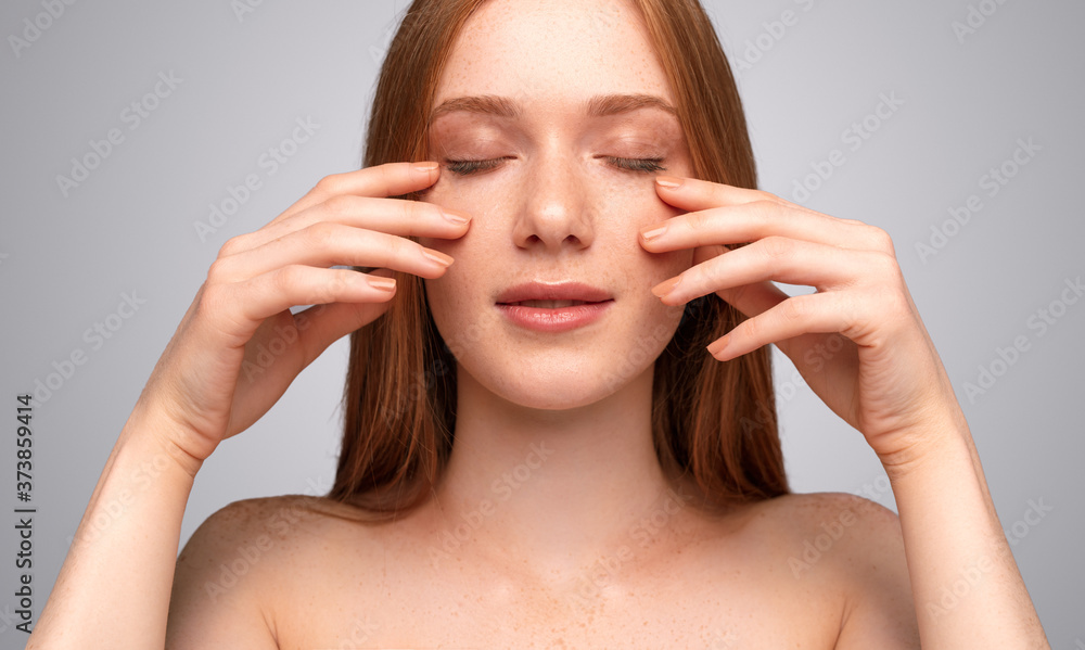 Fototapeta premium Redhead female applying cream on face