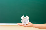 On the palm hand, against the blackboard, is a white alarm clock. Back to school concept.
