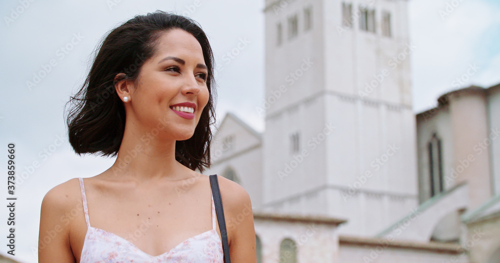Woman walking in rural town square in sunny day.Woman walking and smiling in Assisi square.Woman walking with bell tower in background. Handheld Close up