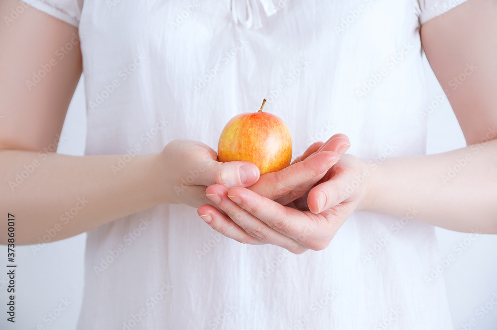 Caucasian woman in a white tunic close-up with an apple in her hands against white background. Caucasian woman in a white tunic close-up with an apple in her hands against white background.