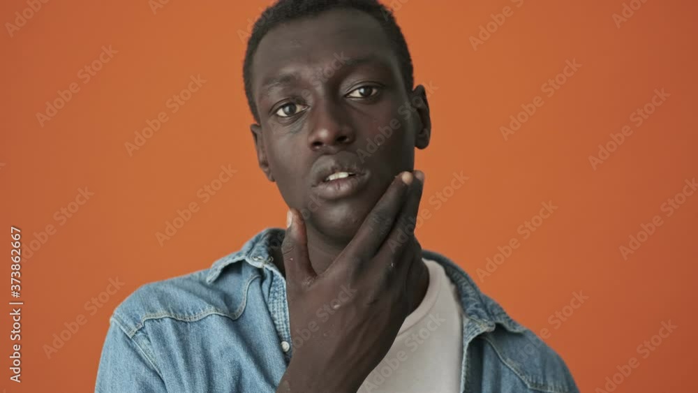 A close-up view of a handsome african american young man looking to the mirror standing isolated over an orange background A close-up view of a handsome african american young man looking to the mirror standing isolated over an orange background