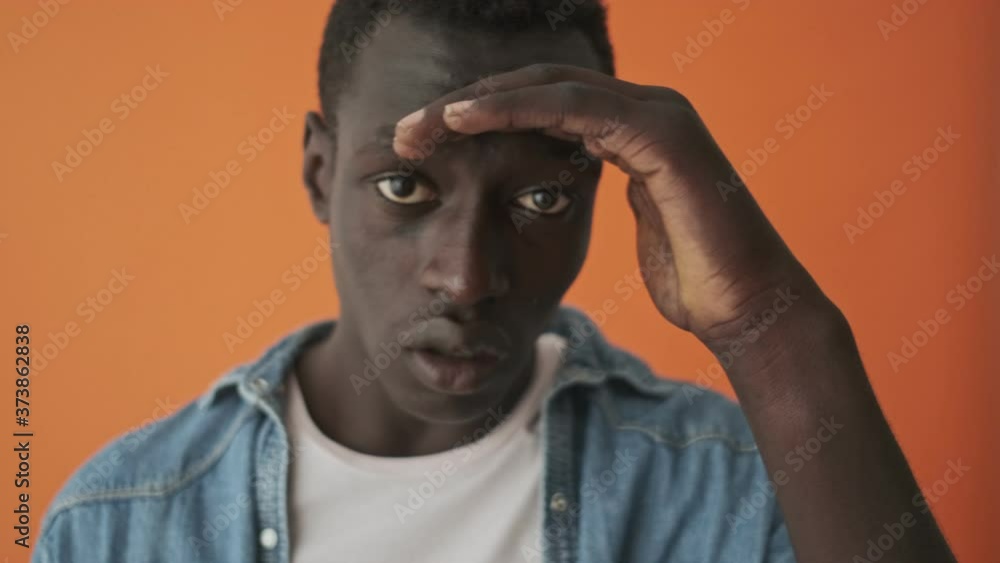 A close-up view of an african american young man is peeping standing isolated over an orange background A close-up view of an african american young man is peeping standing isolated over an orange background