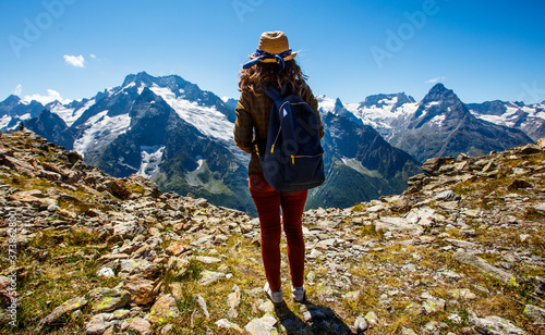 A girl in a hat stands against a background of mountains