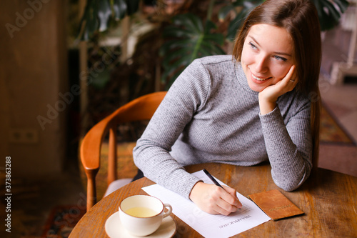 Girl filling visa application, passport and cup on table.