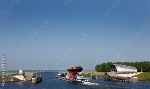 Transport of a super sailing yacht on a pontoon on the river. Keteldiep. Netherlands. Tugboat. Zwarte meer. keteldiep. Ramspol. Balgstuw. Bellows weir.