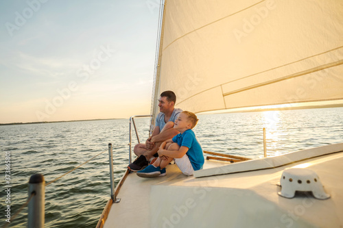 Happy traveler father and son enjoying sunset from deck of sailing boat moving in sea at evening time. Bonding Travel, Summer, Holidays, Journey, Trip, Lifestyle, Yachting concept.  © Andrii IURLOV