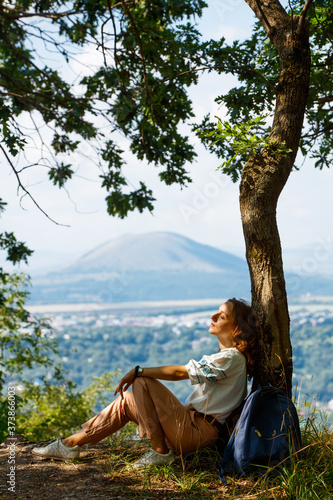 Girl resting by a tree on a mountain background