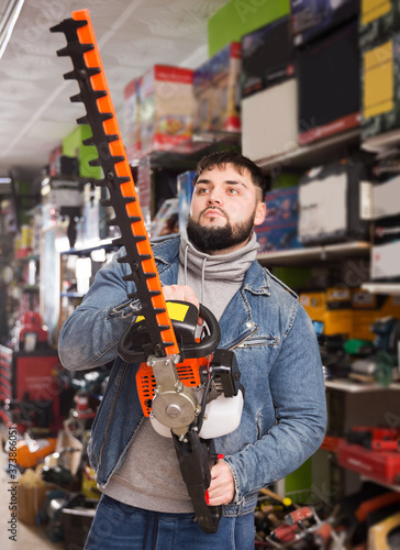 serious man with an electric brush cutter in hardware store