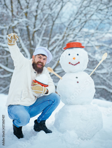 Excited Christmas chef cook. Snowman and funny bearded man in the snow kitchen. Joyful Father cook Having Fun with snowman in Winter Park.