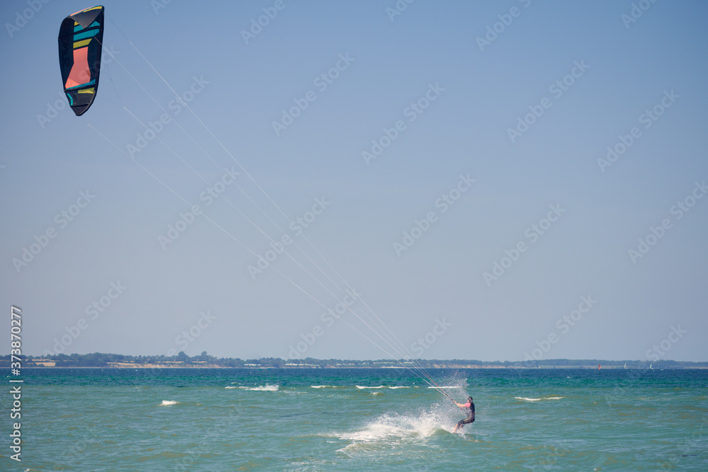 Brunette woman kitesurfing or kite boarding pulling away from the sandy beach making for deeper water on a sunny summer day in a rear view to the camera