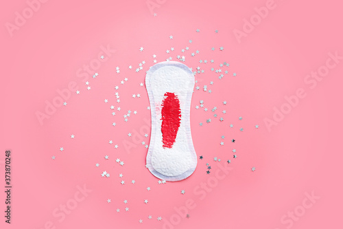 Top view of menstrual daily pad with red blood on it. Pink background and glitter stars. 