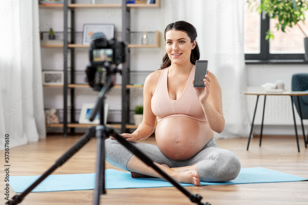 sport, blogging and people concept - happy pregnant woman or blogger with camera on tripod recording online yoga class at home