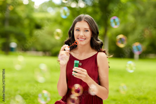 leisure and people concept - portrait of happy smiling woman blowing soap bubbles at summer park