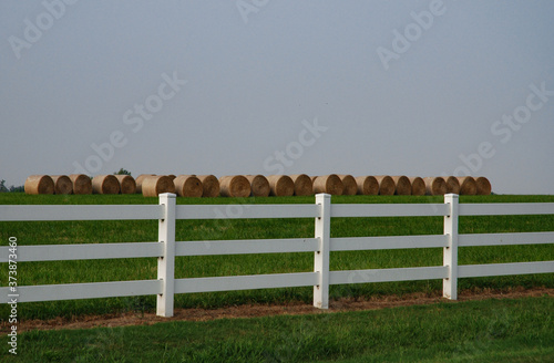 Rural landscape with hayrolls and white fence near Rolla, Missouri, USA.