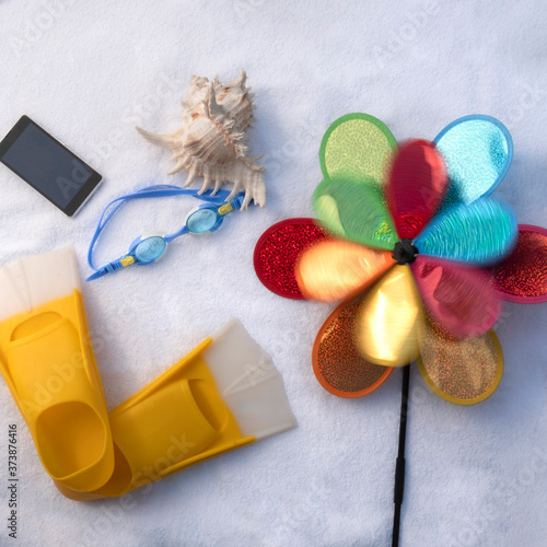 Beach accessories lying on a white towel in the sun, background, flatlay, swimsuit, flip-flops, shell, children's turntable