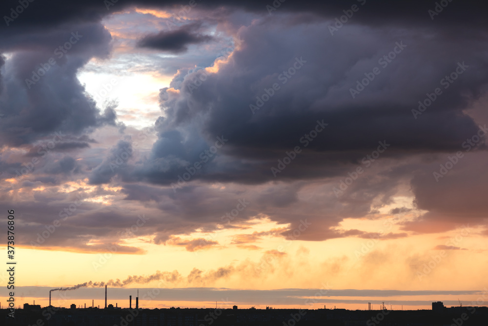 A rainy clouds at the sunset above city buildings silhouette background.