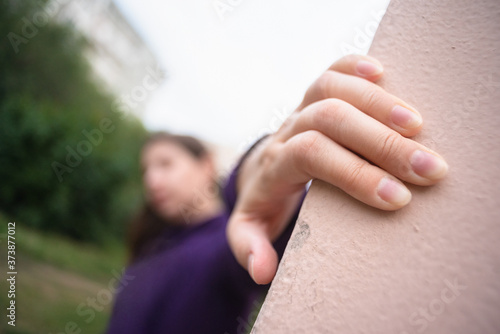 A defocused girl is looking out from a building corner close up.