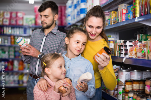 Happy positive family with two little girls buying food products in supermarket