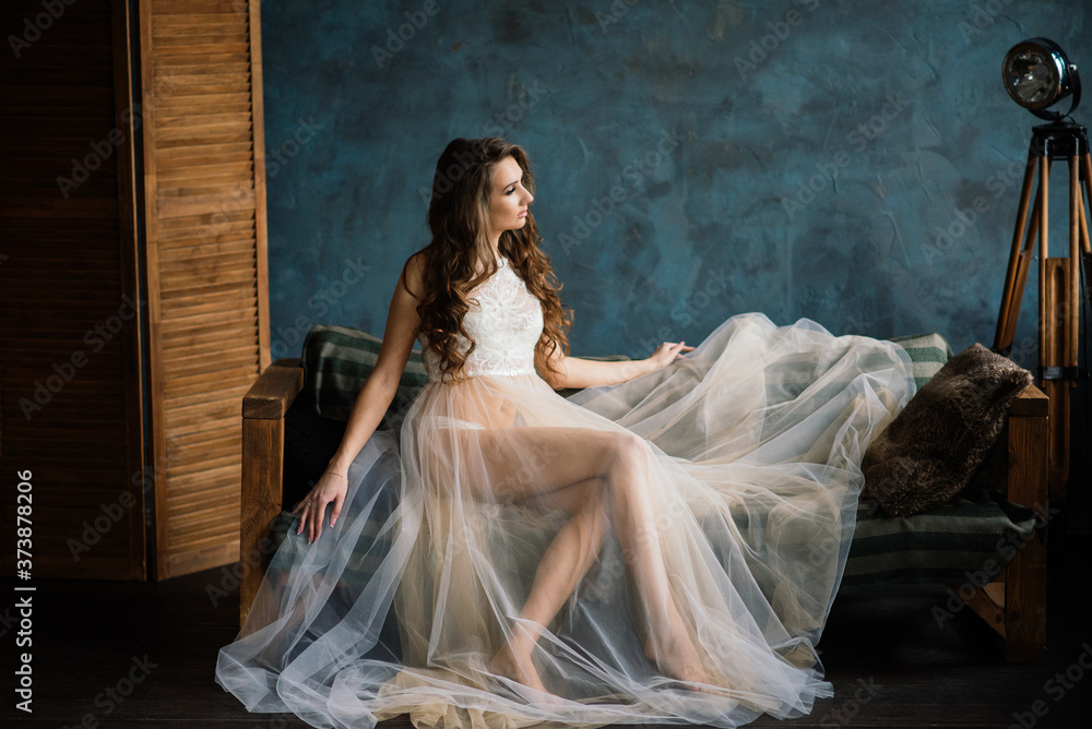 Fototapeta premium Morning of the bride. Sexy girl posing in white lace underwear. Portrait of a beautiful young female in a white underwear. Seductive woman in white linen and a peignoir.