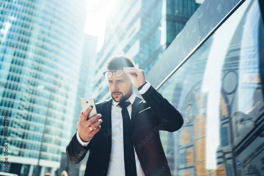 Perplexed businessman in formal suit reading news on smartphone at city street Perplexed businessman in formal suit reading news on smartphone at city street
