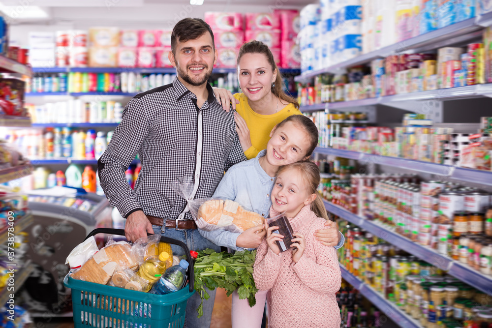 Joyful friendly family of four with full shopping basket in supermarket