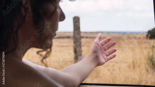  Detail of a woman sticking her hand out the window while driving a van through nature. Road trip