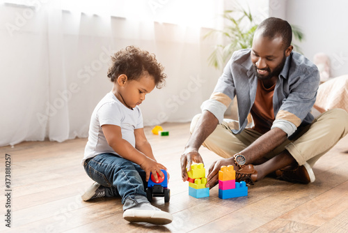 Young African American man playing with building blocks on floor with little son
