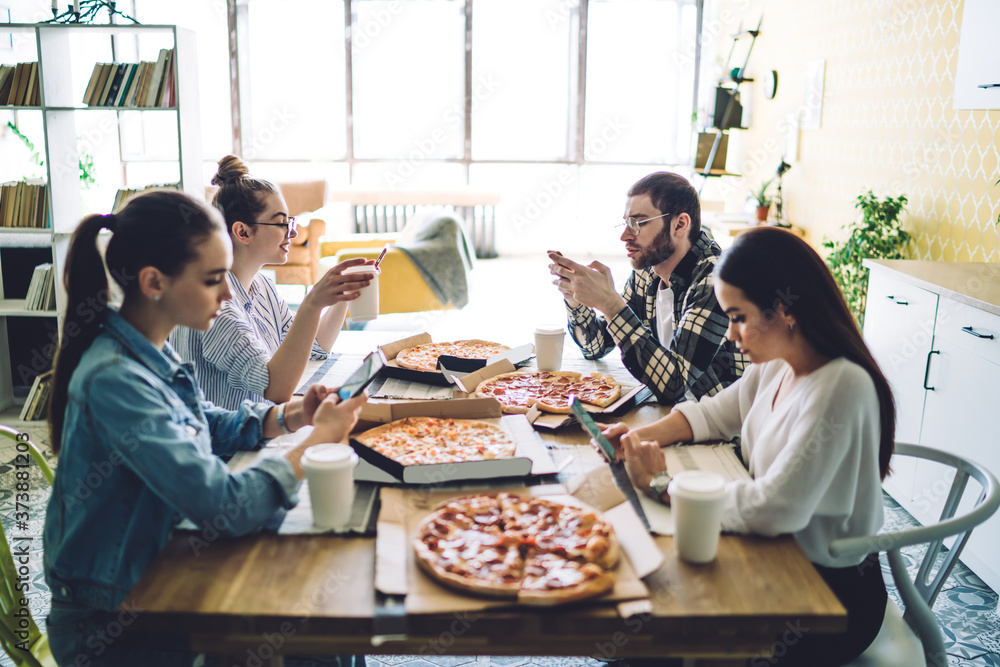 Mates eating pizza and browsing smartphones at table in dining room Mates eating pizza and browsing smartphones at table in dining room
