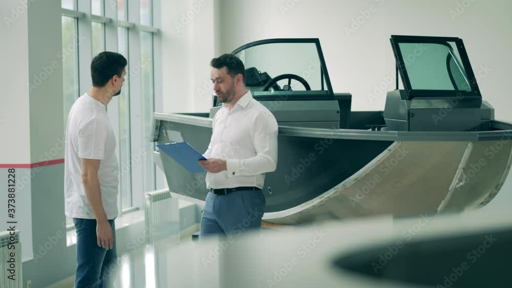 Salesman is talking to a buyer in the motorboat shop Salesman is talking to a buyer in the motorboat shop