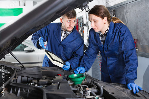 Young female master with foreman are replacing the oil in the car in a workshop