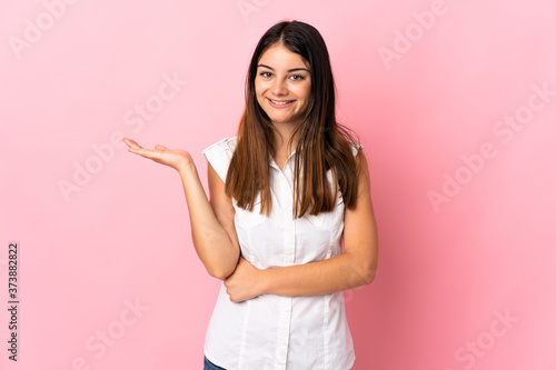 Young caucasian woman isolated on pink background holding copyspace imaginary on the palm to insert an ad © luismolinero