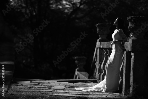 A beautiful bride in a luxurious dress stands on a large balcony. Black and white photo