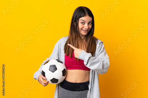 Young caucasian woman isolated on yellow background with soccer ball and pointing to the lateral © luismolinero